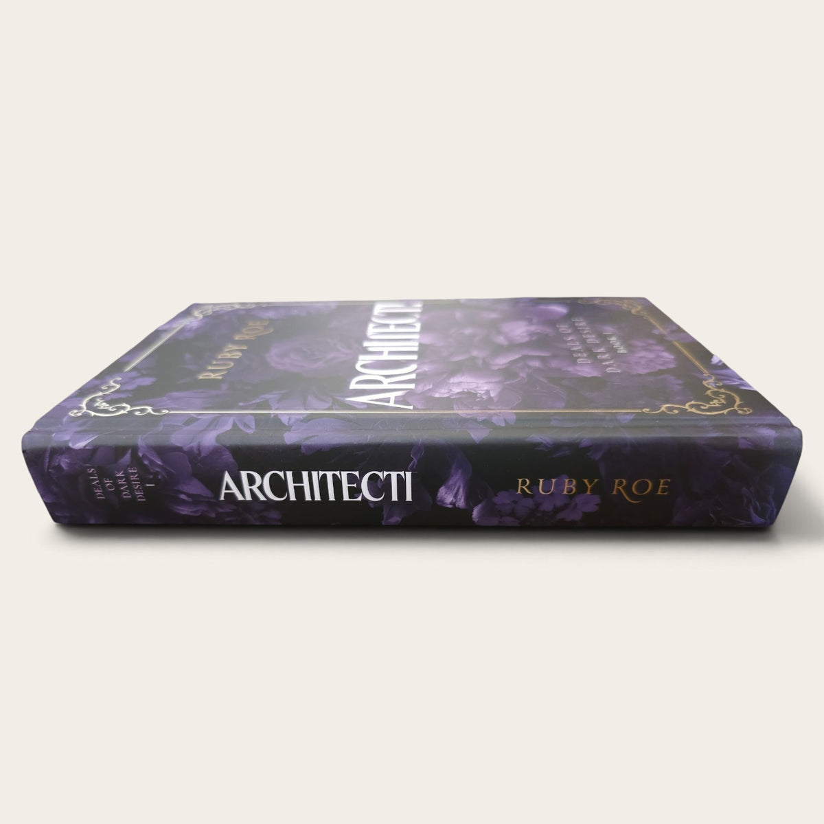A hardcover book titled 'ARCHITECTI' by Ruby Roe, featuring a dark purple floral pattern with gold decorative borders and white and gold lettering on the spine, set against a plain light beige background.
