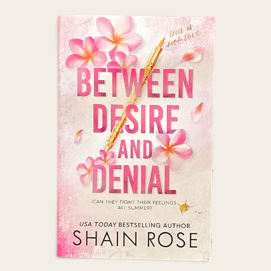 Book cover for 'Between Desire and Denial' by Shain Rose, featuring pink plumeria flowers and a gold pen on a textured light pink and white background.