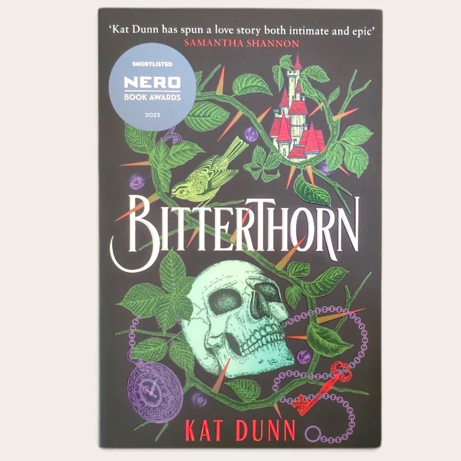 Book cover of 'Bitterthorn' by Kat Dunn, featuring a dark background with a skull, green leaves, thorns, a bird, and a red tower, plus a blue NERO Book Awards shortlist badge.