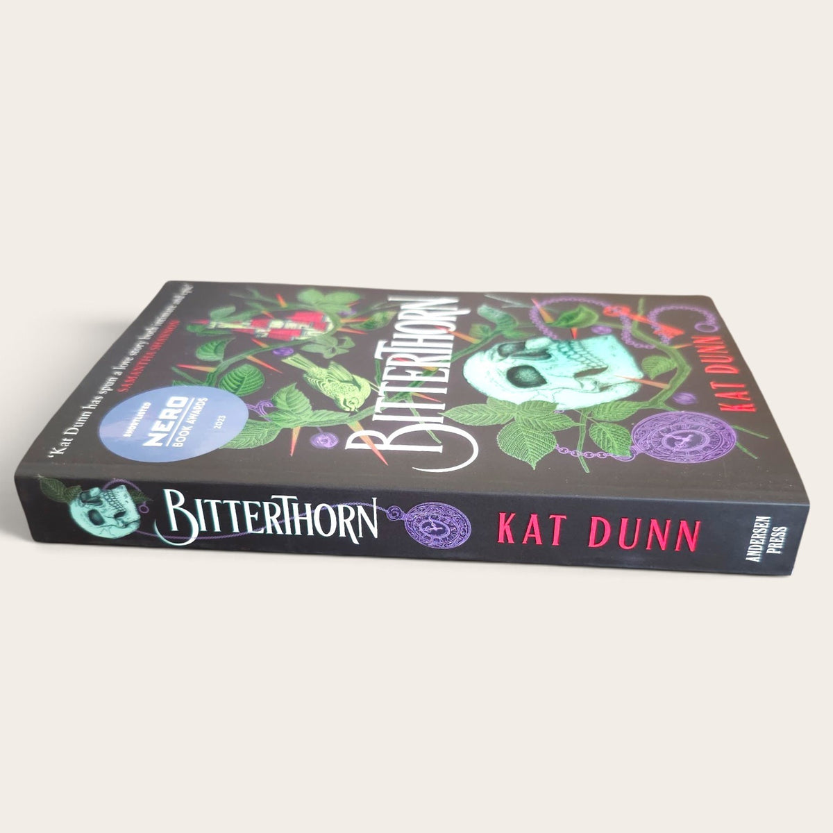 Bitterthorn book by Kat Dunn, published by Anderson Press, featuring a dark cover with a skull, green leaves, and red roses, shown on a light beige background.