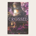 Book cover for 'Crossed' by Emily McIntire, featuring a large bronze bell against a dark background with purple and gold glowing swirls and the title in large metallic letters.