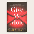 The book cover of 'Give Me More' by Sara Cate, featuring a dark brown and red background with a red rope knot design and white and gold text, shown on a light beige background.