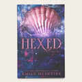 Book cover for 'Hexed: A Never After Novel' by Emily McIntire, featuring a glowing pink shell over a dark blue and purple background