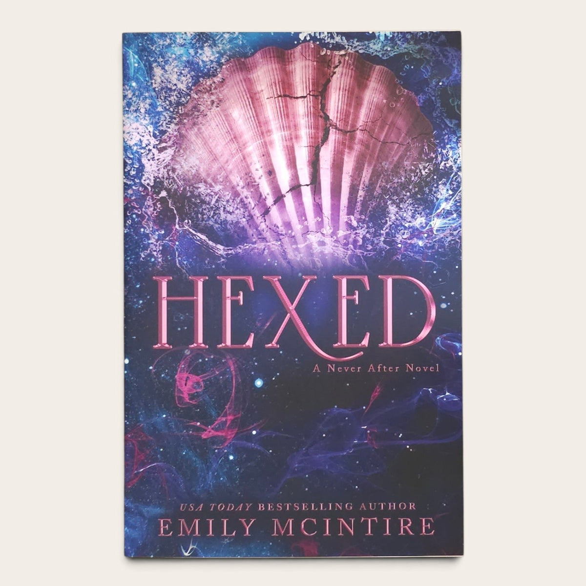 Book cover for 'Hexed: A Never After Novel' by Emily McIntire, featuring a glowing pink shell over a dark blue and purple background