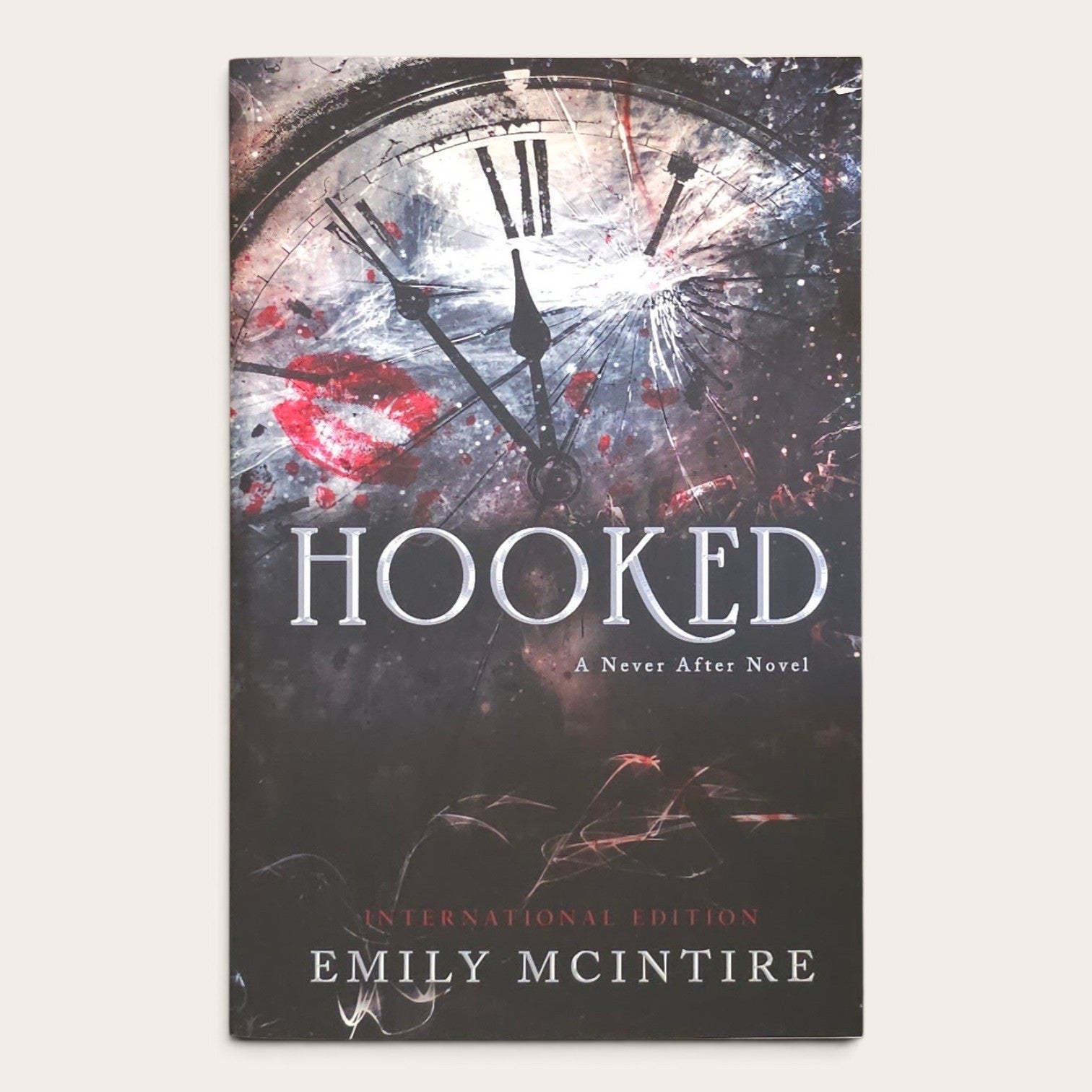 Book cover for 'Hooked: A Never After Novel' by Emily McIntire, featuring a dark clock face with Roman numerals, red lipstick marks, and distressed splatter artwork on a light beige background.