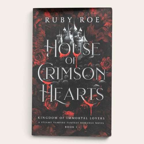 Book cover for 'House of Crimson Hearts' by Ruby Roe, featuring a gothic castle silhouette over a dark background with red roses and red blood-like drips, shown on a light beige background.