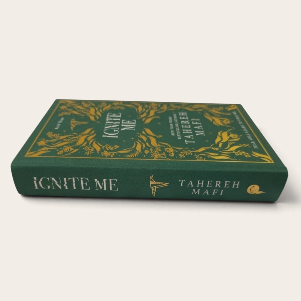 A hardcover book titled 'Ignite Me' by Tahereh Mafi, featuring a dark green cover with ornate gold floral illustrations and gold lettering on the spine, set against a plain off-white background.