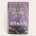 Book cover of 'Interitus' by Ruby Roe, featuring a dark gothic design with purple and black tones, skulls, butterflies, and a central bird silhouette under an ornate archway.