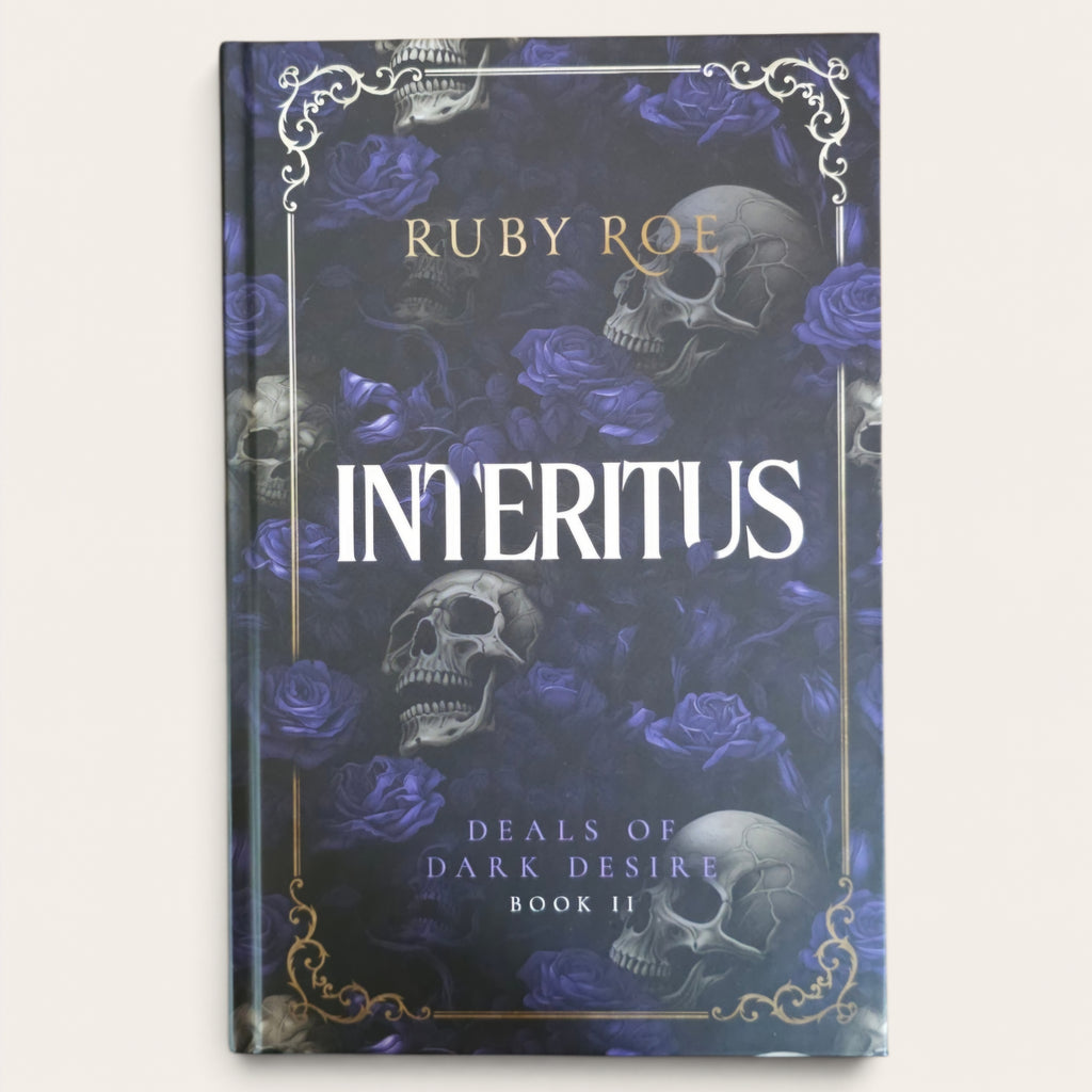 The book cover of 'Interitus: Deals of Dark Desire Book 2' by Ruby Roe, featuring a dark gothic design with purple roses, skulls, and gold ornamental borders on a light beige background.