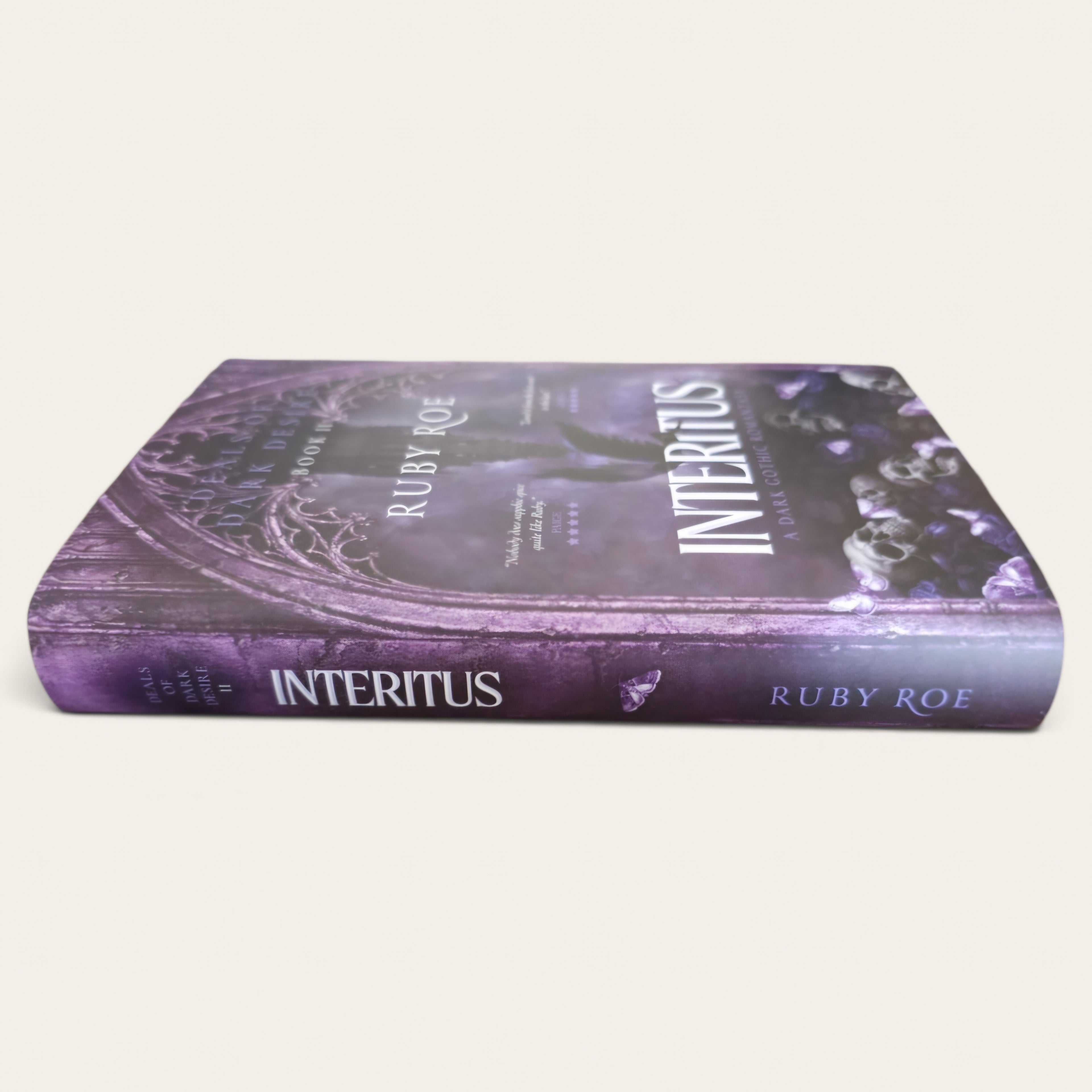A hardcover book titled 'Interitus' by Ruby Roe, featuring a dark purple and black gothic cover design with white title text, photographed on a plain light beige background.