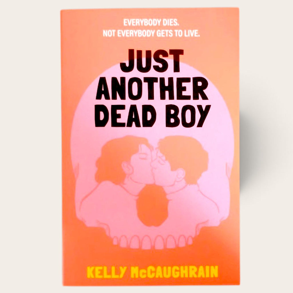 Front cover for Just Another Dead Boy by Kelly McCaughrain. Features a pink skull with 2 people kissing on a bright orange cover. The title is in black, the author name in yellow.