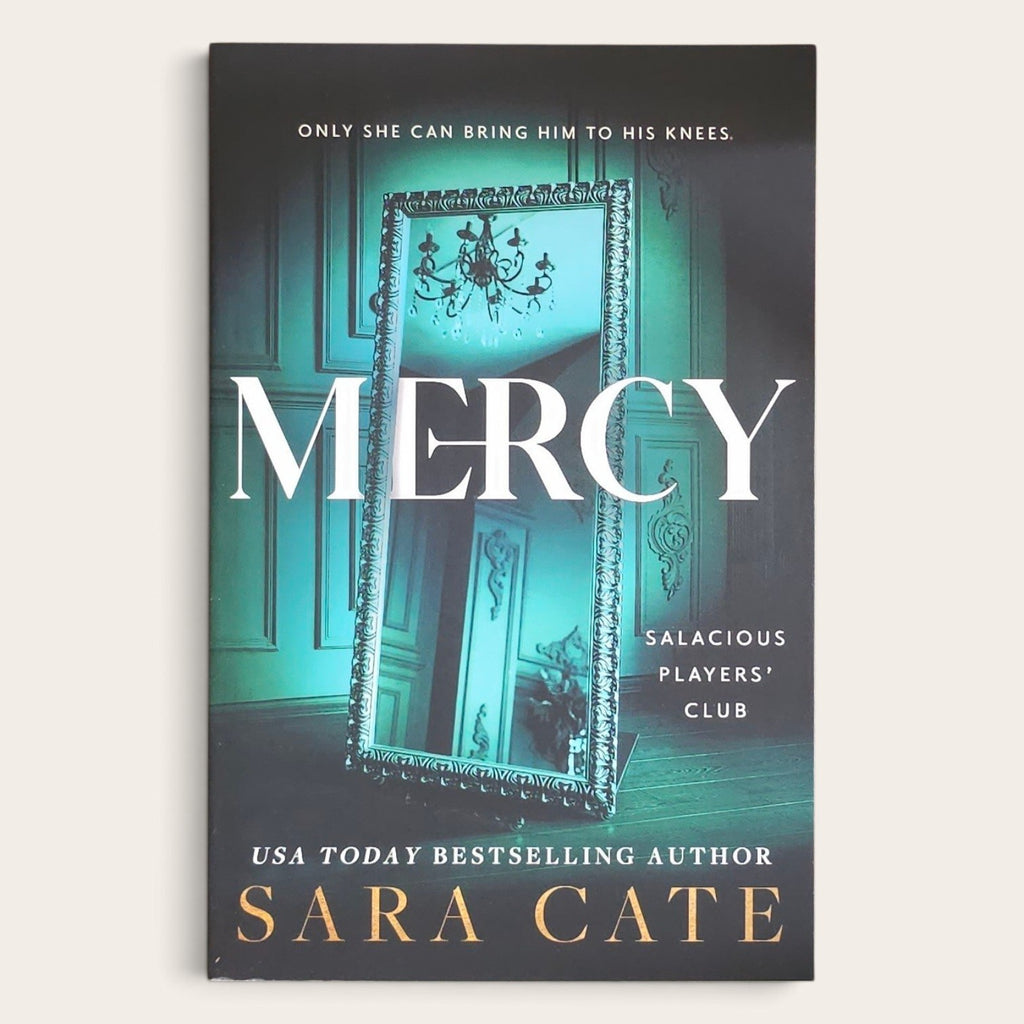 Book cover for 'Mercy' by Sara Cate, featuring a dark teal and black background with a large ornate mirror reflecting an interior scene. The title 'MERCY' is printed in large white letters, with the author name 'SARA CATE' in gold at the bottom.