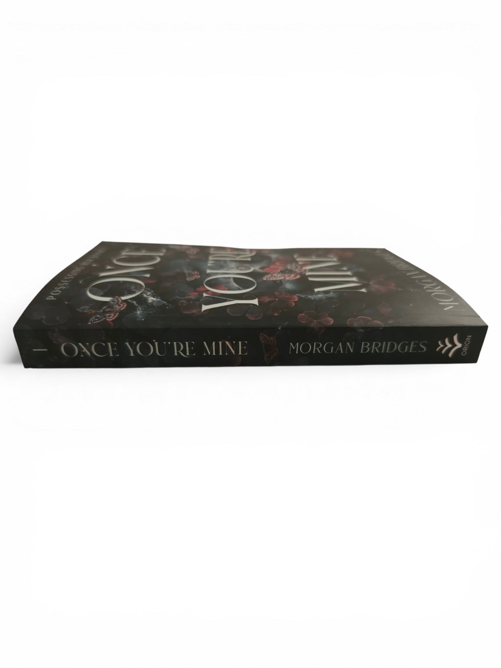 The back and spine of the book 'Once You're Mine' by Morgan Bridges, featuring a dark floral cover design with white lettering, photographed on a clean white background.