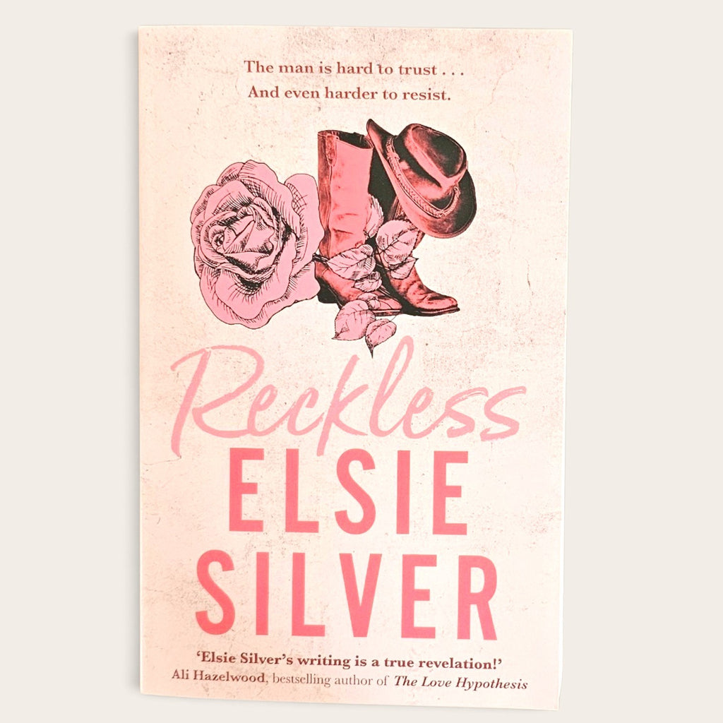Book cover for 'Reckless' by Elsie Silver, featuring a pink and beige western-themed design with a rose, cowboy boots, and hat on a light cream background.