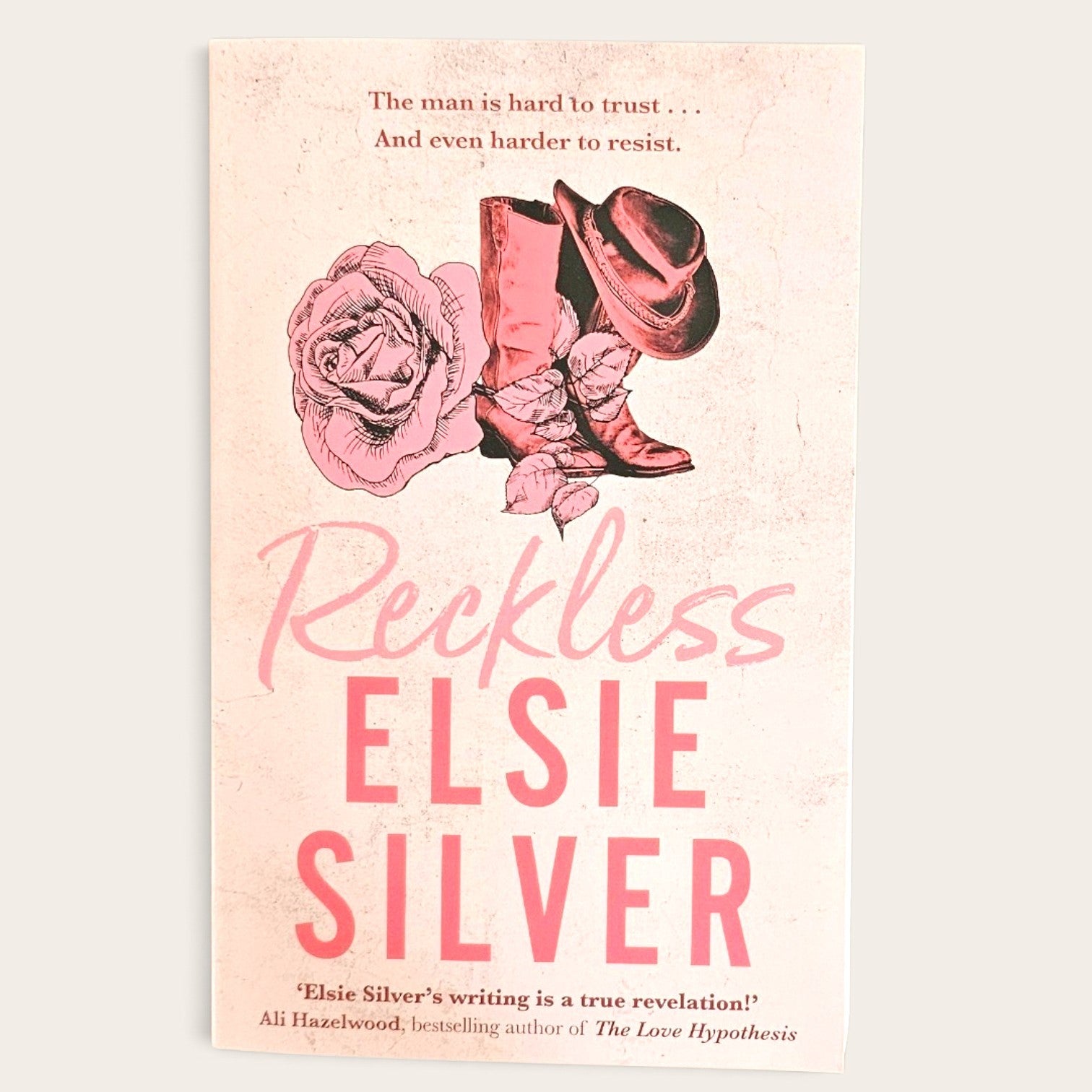 Book cover for 'Reckless' by Elsie Silver, featuring a pink and beige western-themed design with a rose, cowboy boots, and hat on a light cream background.