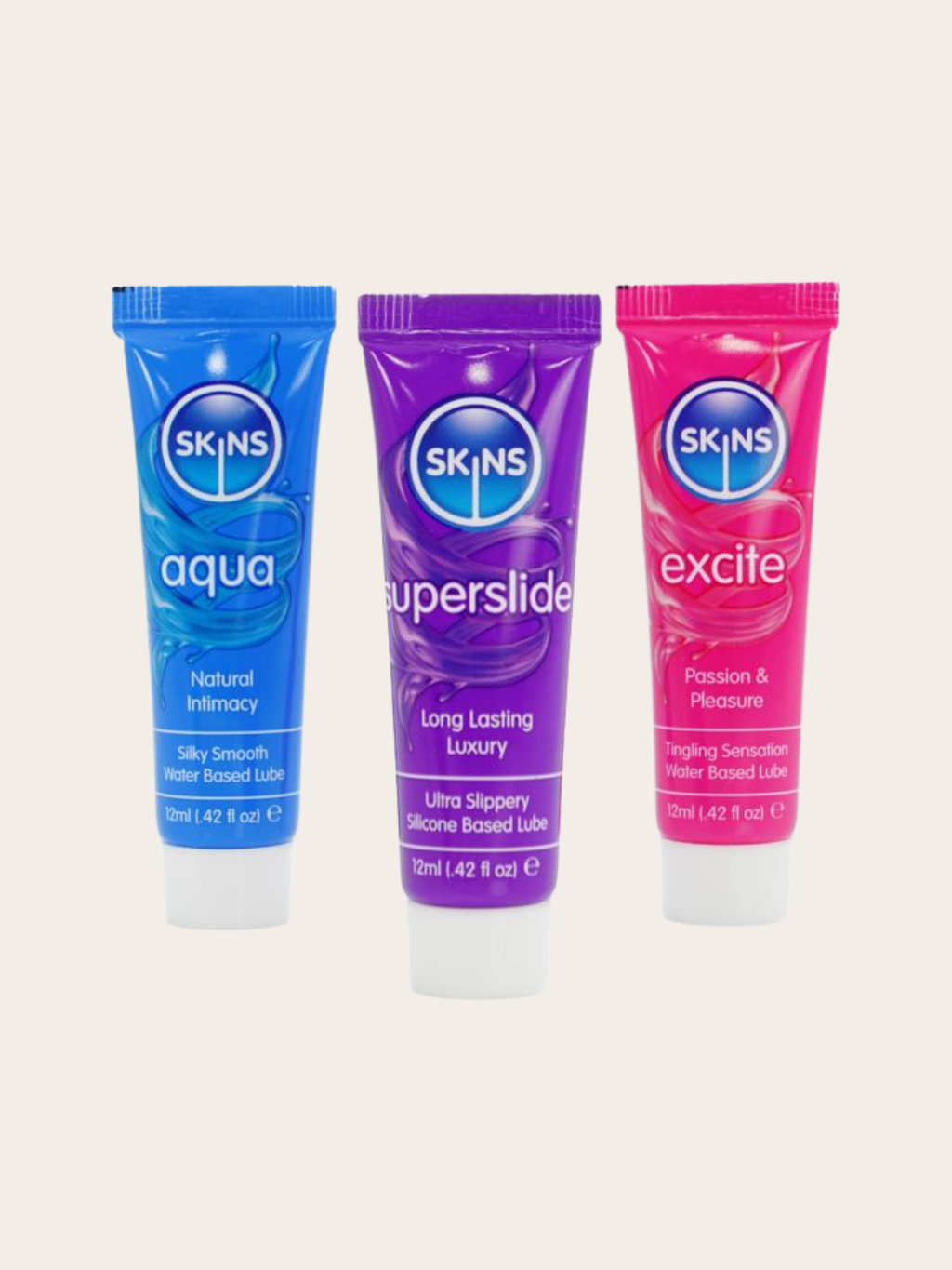 Three SKINS brand lubricant tubes in blue, purple, and pink, arranged side by side on a light beige background.