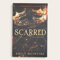 The front cover of the book 'Scarred: A Never After Novel' by Emily McIntire, shown as an International Edition paperback against a light beige background.