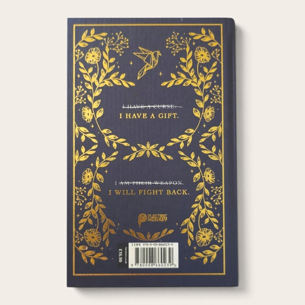 A hardcover book with a dark navy blue cover decorated with gold foil botanical illustrations and text, shown against a light beige background.
