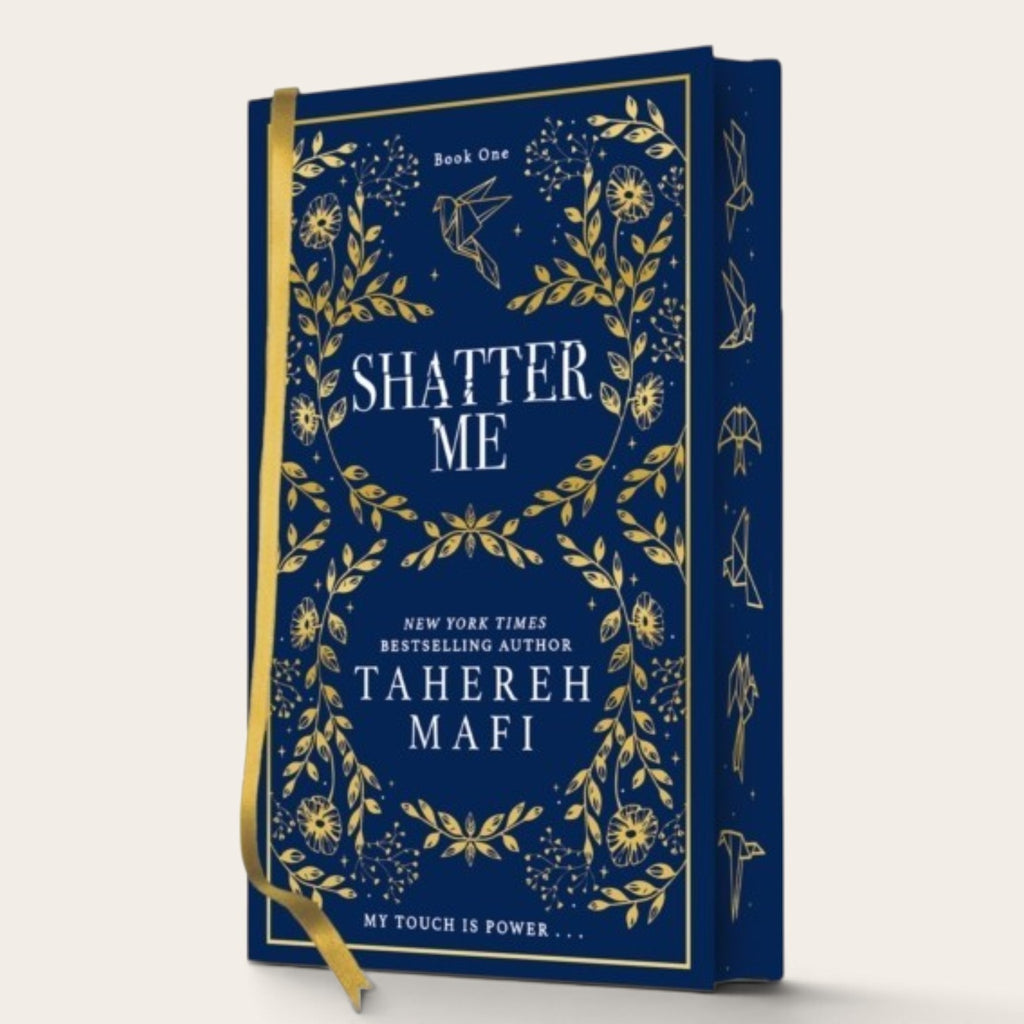Book cover for 'Shatter Me' by Tahereh Mafi, featuring a deep navy blue background with intricate gold botanical illustrations and white typography, complete with a gold ribbon bookmark.