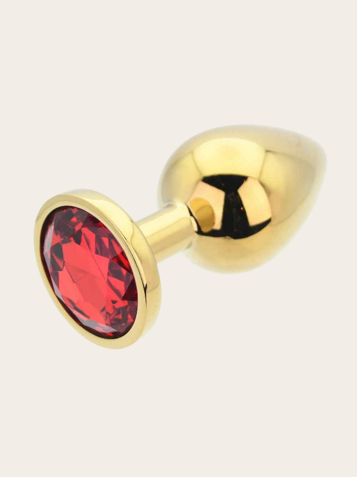 Gold butt plug with a faceted red gemstone accent on the front, shown on a light beige background.