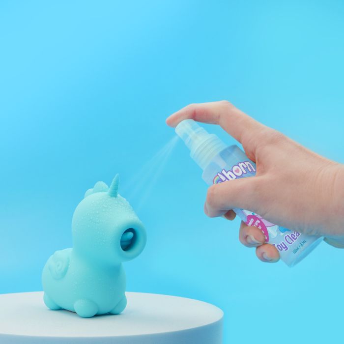 Hand using a spray bottle labeled 'Unihorn Toy Cleaner' on a blue unicorn-shaped object against a blue background