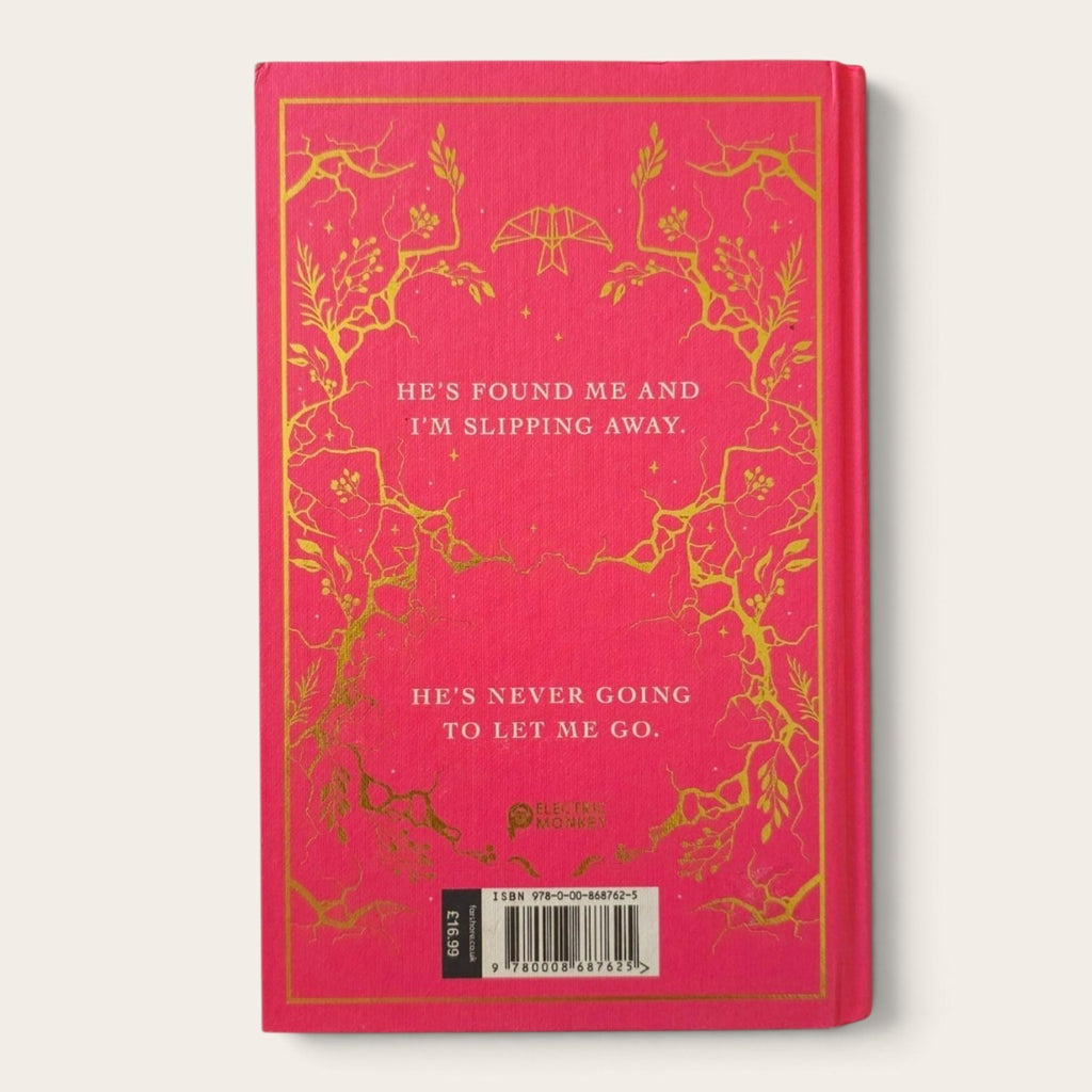 A hardcover book with a bright pink cover and gold foil floral border, featuring white text and a barcode at the bottom, photographed against a light neutral background.