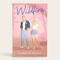 Book cover for 'Wildfire' by Hannah Grace, featuring an illustration of a man and woman standing in front of a pink tree-lined background. The title 'Wildfire' is written in blue script at the top, and the author's name is printed at the bottom.