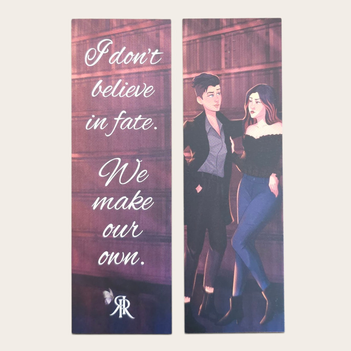 A decorative bookmark showing the front and back, featuring a quote on the left panel and an illustrated couple on the right panel. The left panel reads, 'I don't believe in fate. We make our own.'